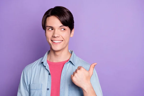Zdjęcie młodego człowieka szczęśliwy pozytywny uśmiech wskazują kciuk puste miejsce polecam promo izolowane na fioletowym tle koloru — Zdjęcie stockowe