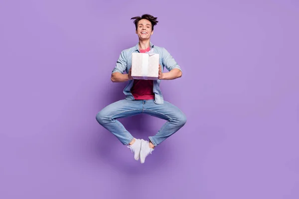 Full size foto van jonge man gelukkig positieve glimlach gast hold huidige doos vliegen lucht sprong geïsoleerd over paarse kleur achtergrond — Stockfoto