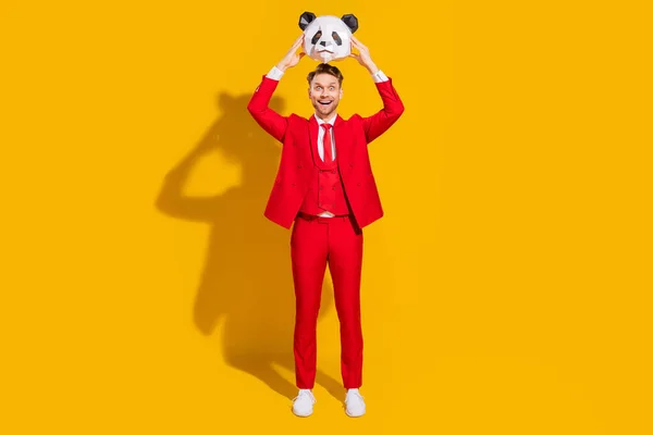 Foto di eccitato stupito intrattenitore ragazzo tenere panda testa bocca aperta indossare cravatta tuta rossa isolato su sfondo di colore giallo — Foto Stock