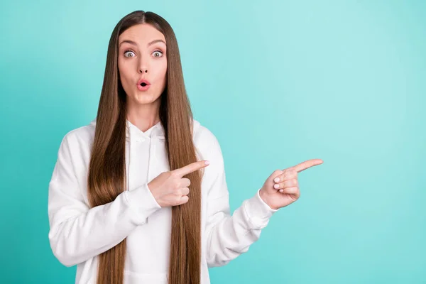 Foto de linda mujer joven impresionada vestida con capucha blanca sosteniendo los dedos apuntando espacio vacío color verde azulado fondo — Foto de Stock