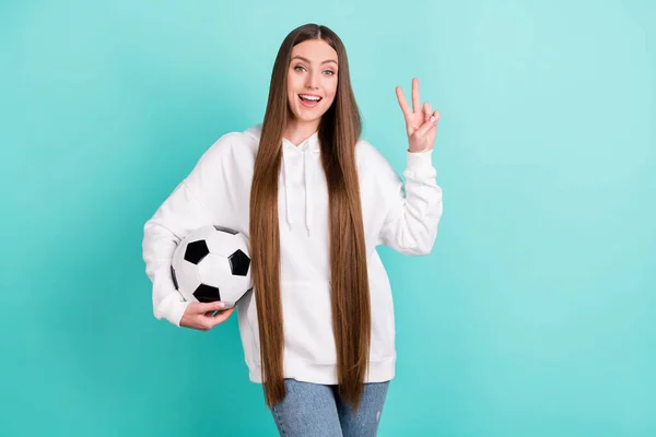 Fotografie pozitivní šťastná mladá žena držet ruční fotbal, aby V-znamení izolované na pastel teal barva pozadí — Stock fotografie