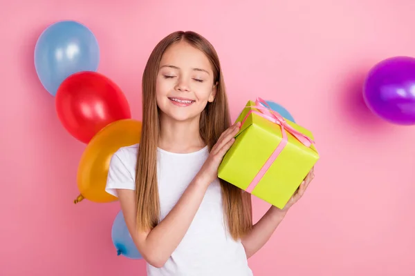 Foto van mooie blonde kleine meisje houden aanwezig gesloten ogen dragen witte t-shirt geïsoleerd op roze kleur achtergrond — Stockfoto