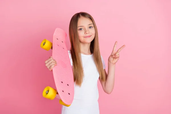 Фото фанки блондинка маленькая девочка показать V-знак держать скейт носить белые футболки изолированы на розовом фоне цвета — стоковое фото