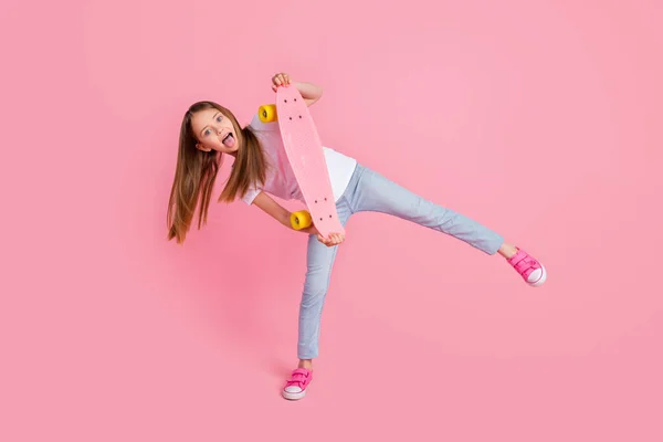 Фотографія повної довжини смішної блондинки маленької дівчинки язик тримає скейт одяг білої футболки джинси ізольовані на рожевому кольоровому фоні — стокове фото