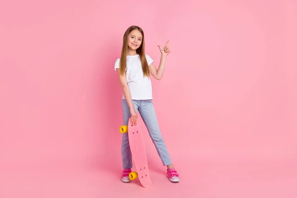 Full body fotografie pěkné blond holčička držet brusle bod prázdný prostor nosit bílé tričko džíny izolované na růžové barevné pozadí — Stock fotografie