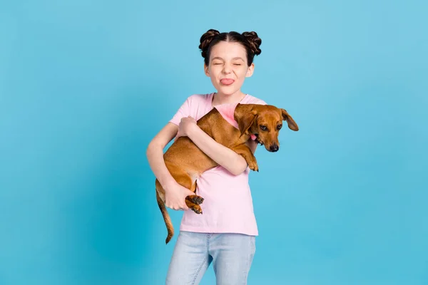 Foto di allegro giovane giocoso piccola ragazza bastone fuori lingua funky tenere cane isolato su sfondo di colore blu — Foto Stock