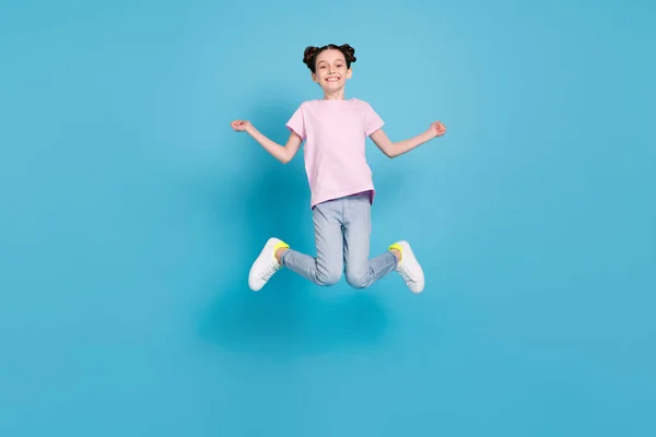 Foto av bedårande söt skolflicka klädd rosa t-shirt hoppa högt leende isolerad blå färg bakgrund — Stockfoto