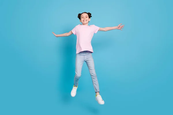 Photo of charming pretty school girl nosić różowy t-shirt uśmiechnięty skoki wysokie ramiona boki odizolowane niebieski kolor tła — Zdjęcie stockowe