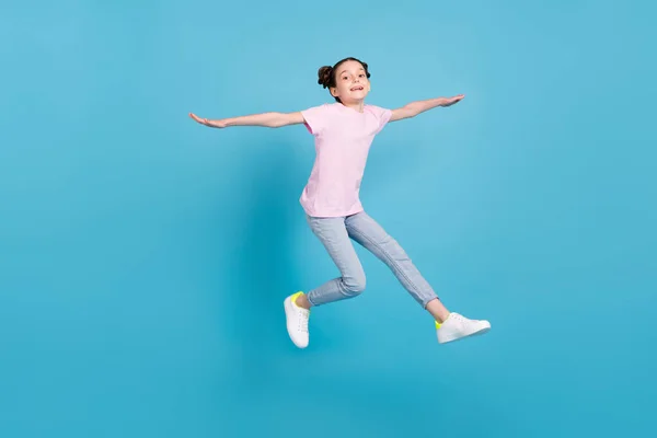 Foto van grappig charmant schoolmeisje gekleed roze t-shirt armen zijden springen hoog glimlachen geïsoleerde blauwe kleur achtergrond — Stockfoto