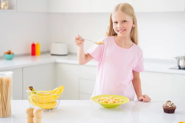 Foto di giovane attraente bambina felice sorriso positivo colazione mangiare fiocchi di mais cucchiaio nutrizione cibo al chiuso — Foto Stock