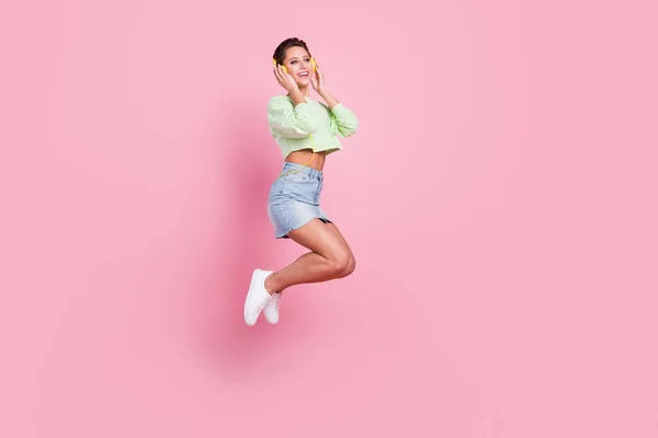 Full body photo of happy nice positive woman jump up smile listen music headset isolated on pink color background