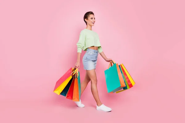 Full body profil boczny zdjęcie młodej atrakcyjnej dziewczyny szczęśliwy pozytywny uśmiech iść spacer kupujący shopper izolowane na pastelowym tle kolor — Zdjęcie stockowe