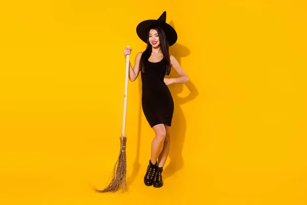 全身上下都是滑稽的巫女，戴着扫帚，头戴黑色连衣裙，背景是黄色的 — 图库照片