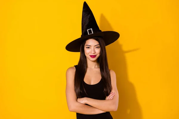 Foto de señora bruja bonita cruzó brazos usar gorra de vestido negro aislado en el fondo de color amarillo —  Fotos de Stock