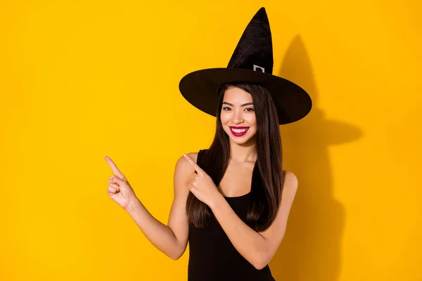 Foto von optimistischen Millennial Brünette Frisur Dame Punkt leeren Raum tragen schwarzes Kleid Hexenmütze isoliert auf gelbem Hintergrund — Stockfoto