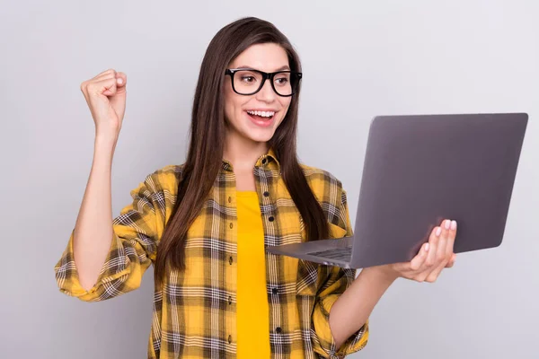 Фото молодой веселой женщины счастливой позитивной улыбкой смотреть ноутбук праздновать победу изолированы на сером фоне — стоковое фото