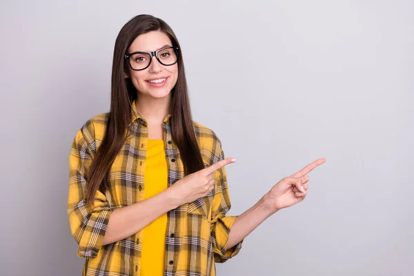 Фото молодой девушки счастливая положительная улыбка указывает пальцами пустое пространство реклама выбрать изолированный на сером фоне цвета — стоковое фото