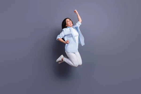 Foto de comprimento total de brilhante sorte jovem senhora vestida camisa azul pulando levantando punhos isolado fundo cor cinza — Fotografia de Stock