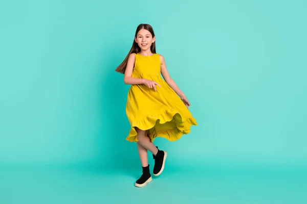 Foto penuh gadis rambut coklat yang optimis menari mengenakan sepatu gaun kuning terisolasi di latar belakang warna teal cerah — Stok Foto
