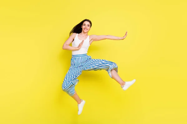 フルサイズの写真の面白いブルネット女性ジャンプ着用トップパンツスニーカー絶縁で黄色の色の背景 — ストック写真
