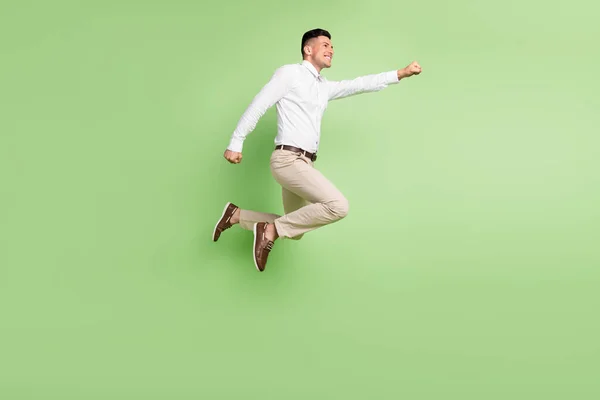 Foto de comprimento total de bonito cavalheiro engraçado usar camisa branca sorrindo pulando alto olhando espaço vazio isolado cor verde fundo — Fotografia de Stock