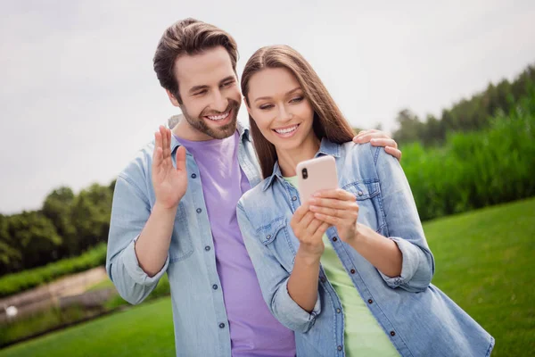 Foto de buen humor encantadora pareja bonita relajarse al aire libre hablando con amigos cámara web en el teléfono inteligente disfrutar de fin de semana —  Fotos de Stock