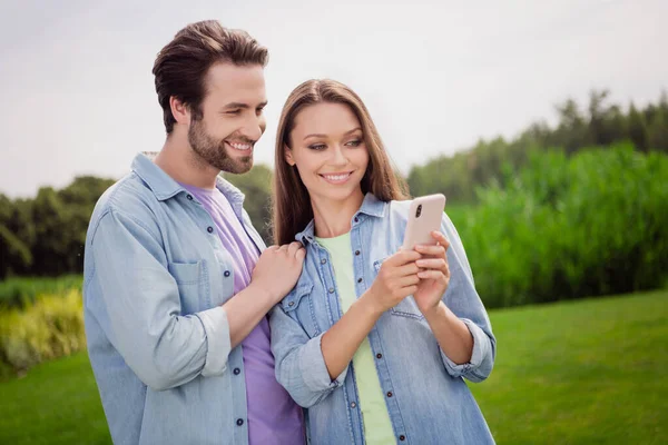 Foto de sonriente alegre encantadora pareja bonita relajarse al aire libre utilizando el teléfono inteligente navegar en Internet disfrutando de fin de semana — Foto de Stock