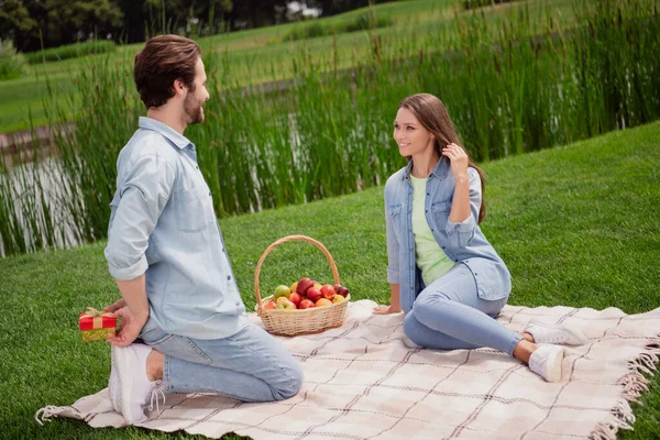 照片上的好心情微笑迷人的年轻夫妇在户外放松有野餐在公园男朋友背后藏着礼物 — 图库照片