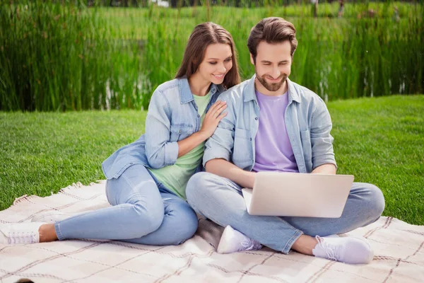 Full size photo of cheerful positive married couple sit grass outside browsing in laptop watch video movie relaxing outdoors — Stock Photo, Image