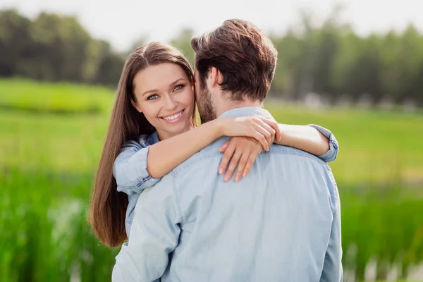Фото позитивно улыбающейся веселой жены обнимающей мужа, наслаждающейся медовым месяцем на открытом воздухе, расслабляющей — стоковое фото