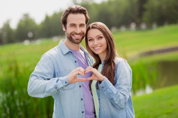 Foto de buen humor positivo encantadora pareja mostrar los dedos del corazón disfrutando de luna de miel celebrar aniversario al aire libre —  Fotos de Stock