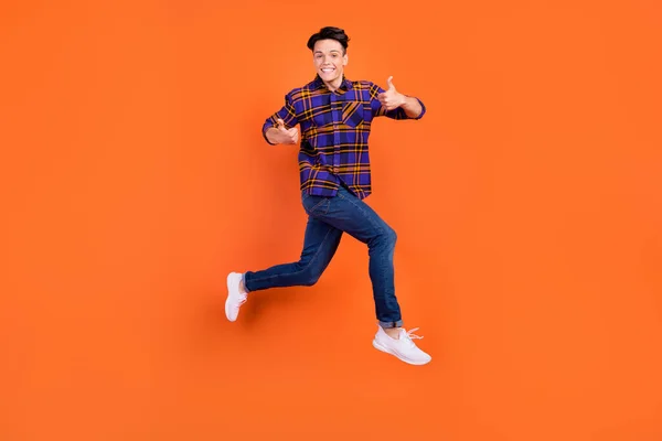 Full size profile photo of young cool guy jump show thumb up wear shirt jeans sneakers isolated on orange background — Stock Photo, Image