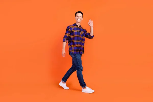 Foto de perfil de cuerpo completo de un joven lindo tipo ir onda usar camisa jeans zapatillas aisladas sobre fondo naranja —  Fotos de Stock