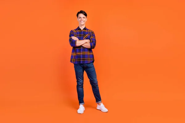 Volledige lengte foto van millennial leuke man staan gekruiste armen dragen shirt jeans sneakers geïsoleerd op oranje achtergrond — Stockfoto