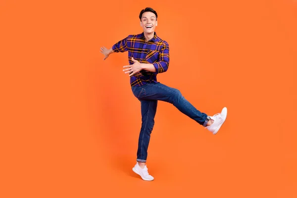 Foto de divertido bastante adolescente vestido a cuadros ropa bailando sonriente aislado color naranja fondo — Foto de Stock