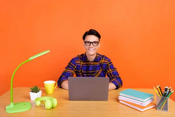 Foto de milenar cara legal escrever laptop desgaste xadrez camisa óculos isolados no fundo cor de laranja — Fotografia de Stock