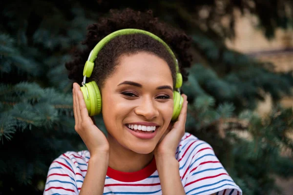 Φωτογραφία της νεαρής χαρούμενης μαύρης γυναίκας χαρούμενο θετικό χαμόγελο Απολαύστε ακρόαση μουσική ακουστικά φύση σε εξωτερικούς χώρους — Φωτογραφία Αρχείου