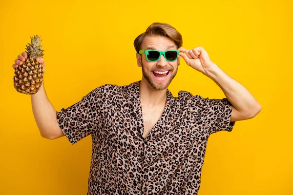 Photo de doux charmant jeune homme habillé chemise bras lunettes sombres tenant ananas isolé fond de couleur jaune — Photo