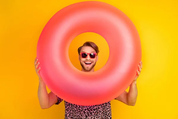 Photo of charming impressed young guy wear leopard outfit dark eyewear looking inflatable buoy isolated yellow color background