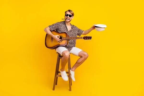 Foto di carino giovane ragazzo indossare abito leopardo occhiali scuri chiedendo consigli cappello fumare suonare la chitarra isolato colore giallo sfondo — Foto Stock