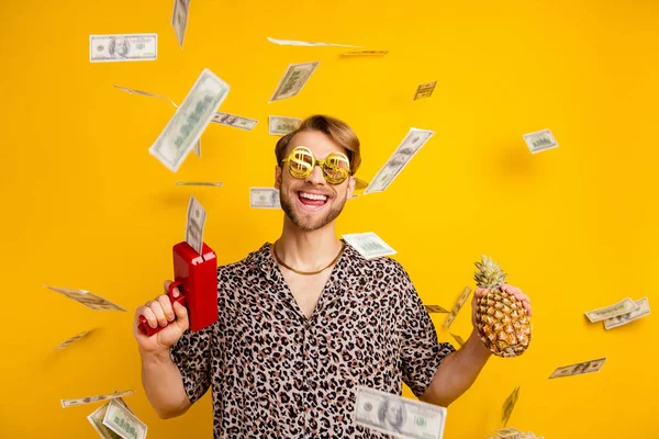 Foto de cara engraçado doce usar roupa de leopardo óculos segurando abacaxi disparando arma dinheiro isolado cor amarela fundo — Fotografia de Stock