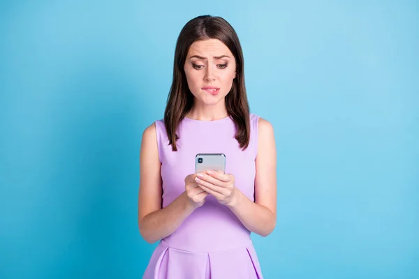 Foto de mujer bastante joven asustada sostener teléfono morder los dientes del labio desgaste traje violeta aislado en fondo de color azul — Foto de Stock