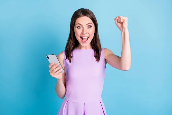 아름다운 행복 한 승리의 사진 주먹을 들고 있는 젊은 여성 파란 배경 위에 고립된 스마트폰 메시지를 들고 있어요 — 스톡 사진