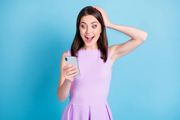 Photo of amazed happy young woman trzymać głowę wygląd telefonu wiadomość nosić fioletowy strój odizolowany na niebieskim tle koloru — Zdjęcie stockowe