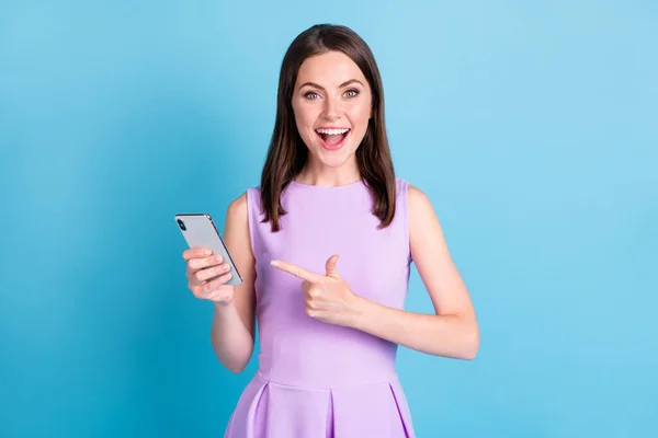 Fotografie užaslý šťastný veselá mladá žena ukazováček držet chytrý telefon izolovat na lesk modré barvy pozadí — Stock fotografie