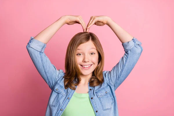 Foto retrato menina sorrindo mostrando sinal de coração com as mãos isolado pastel cor-de-rosa fundo — Fotografia de Stock