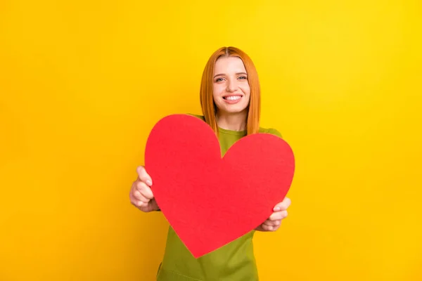 Foto de cabelo vermelho romântico jovem senhora segurar coração desgaste camisola verde isolado no fundo de cor amarela — Fotografia de Stock