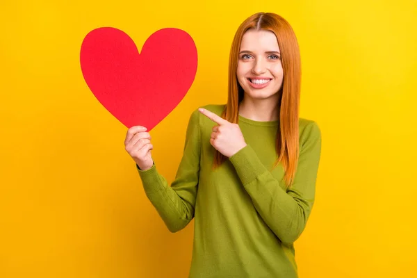 Foto de bonito penteado vermelho millennial senhora ponto coração desgaste camisola verde isolado no fundo de cor amarela — Fotografia de Stock