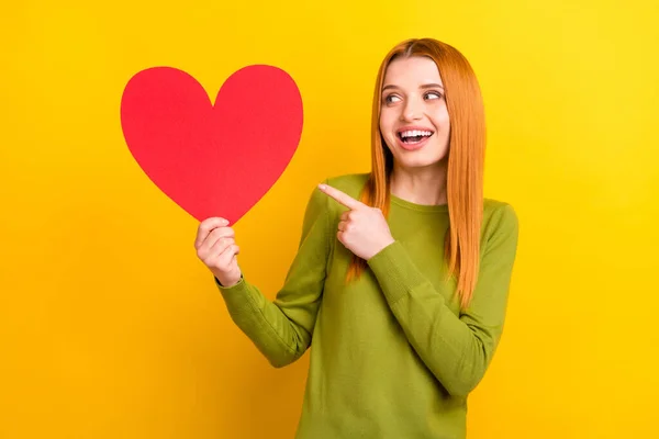 Foto de engraçado gengibre penteado jovem senhora ponto olhar coração desgaste verde suéter isolado no fundo de cor amarela — Fotografia de Stock