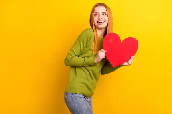 Foto van funky rood kapsel jonge dame houden hart kijken lege ruimte dragen groene trui geïsoleerd op gele kleur achtergrond — Stockfoto